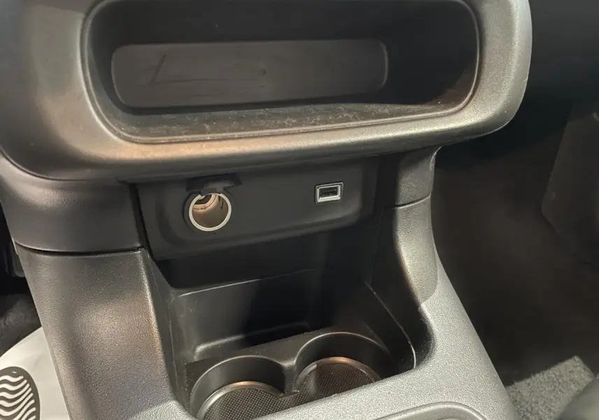 Gros plan sur la console centrale noire avec prise USB et allume-cigare dans une Citroën C3 gris foncé.
