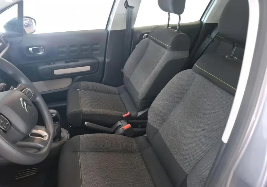 Vue intérieure côté conducteur de la Citroën C3 2024 gris foncé, montrant les sièges avant en tissu avec surpiqûres jaunes.