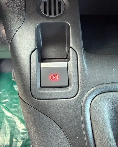 Gros plan sur le bouton de frein à main électronique rouge dans l'habitacle noir du Citroën Berlingo blanc 2026.