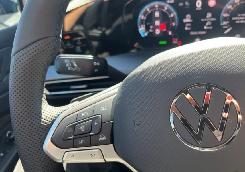 Gros plan sur le volant cuir multifonctions de la Volkswagen Golf TDI 150 R-Line, avec tableau de bord numérique en arrière-plan.