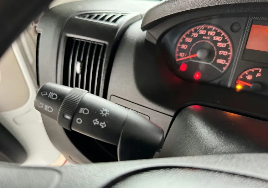 Gros plan sur le commodo des feux et le tableau de bord éclairé du Citroën Jumper Benne rouge, intérieur noir.