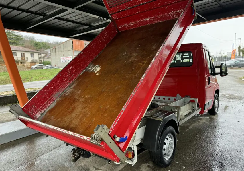 Vue 3/4 arrière droite d'un Citroën Jumper benne rouge avec plateau basculant relevé et attelage visible.