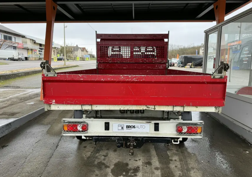 Vue arrière d’un Citroën Jumper benne rouge avec ridelles latérales et attelage visible sous abri.