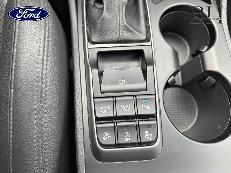 Vue rapprochée de la console centrale noire avec commandes électroniques de frein à main et modes de conduite.