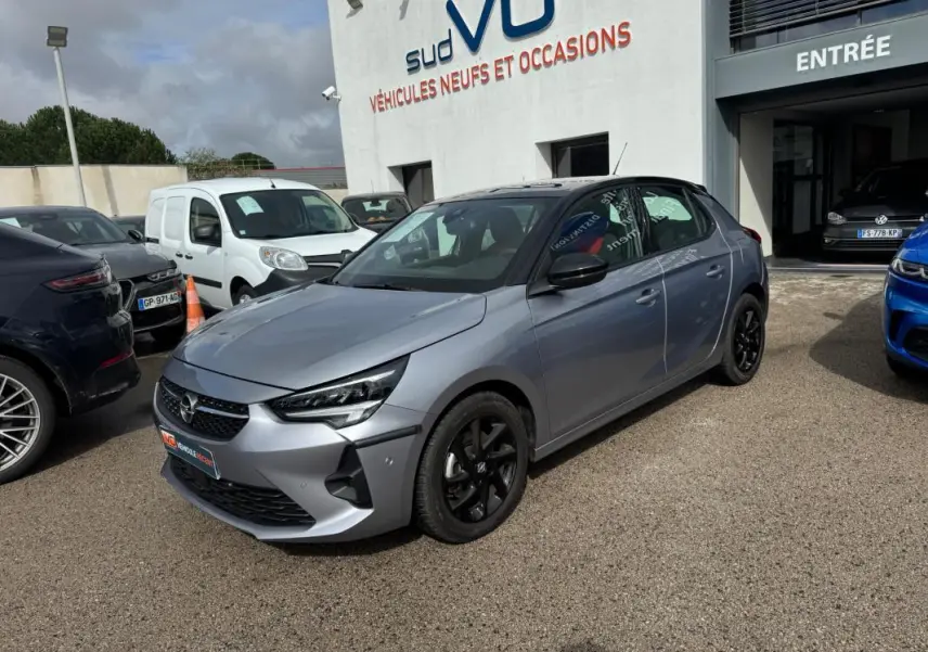 Opel Corsa 1.2 Turbo gris clair vue 3/4 avant droit avec jantes noires, stationnée devant un concessionnaire.