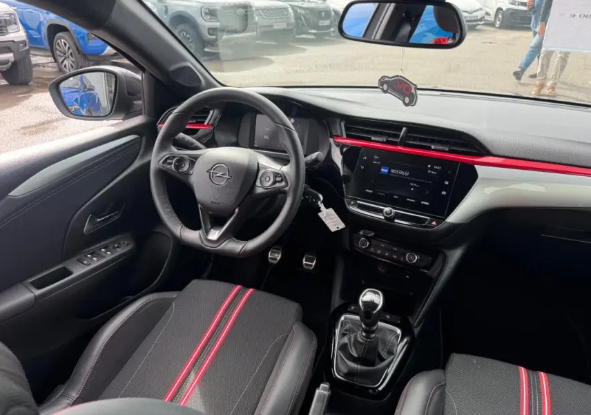 Vue intérieure côté conducteur de l’Opel Corsa gris clair 2022, avec volant, tableau de bord et sièges noirs à bandes rouges.