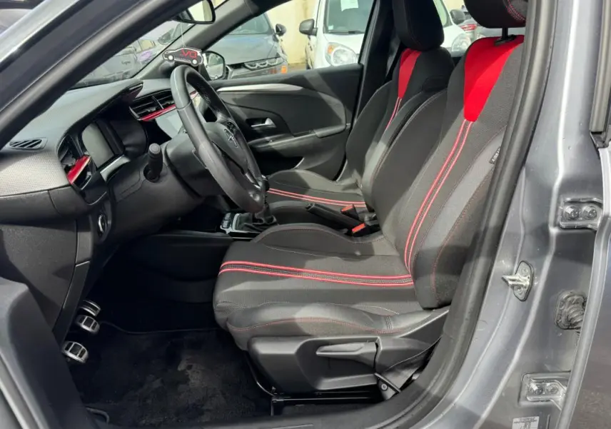 Vue intérieure côté conducteur de l’Opel Corsa gris clair 2022, sièges noirs avec surpiqûres rouges et volant multifonction.