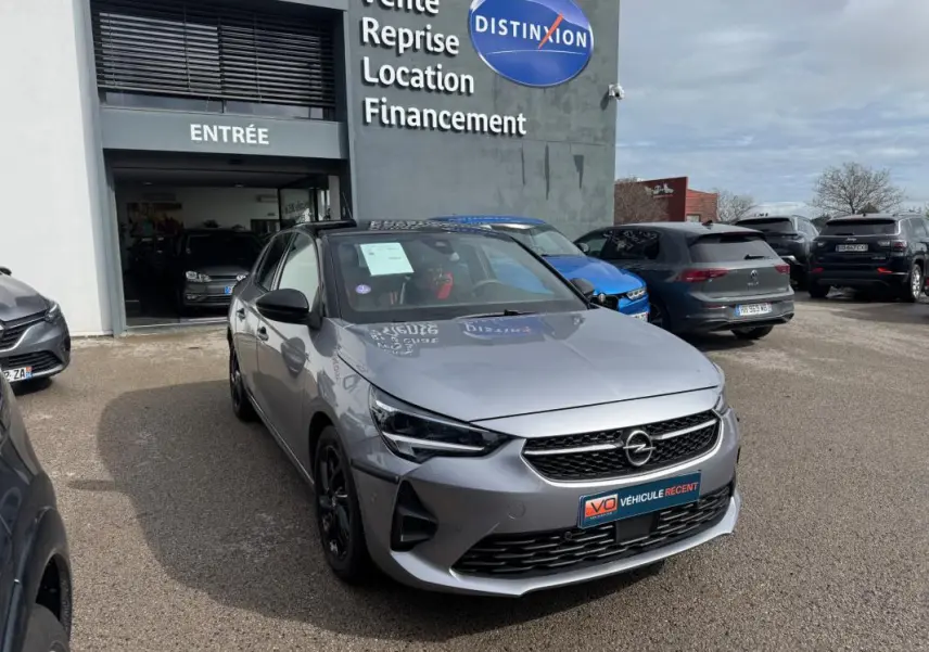 Opel Corsa gris clair vue 3/4 avant droit, calandre noire et jantes foncées, devant un garage Distinxion.