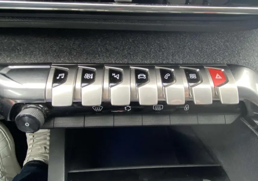 Gros plan sur la rangée de boutons argentés et rouges de la console centrale d’un Peugeot 3008 blanc, intérieur noir.