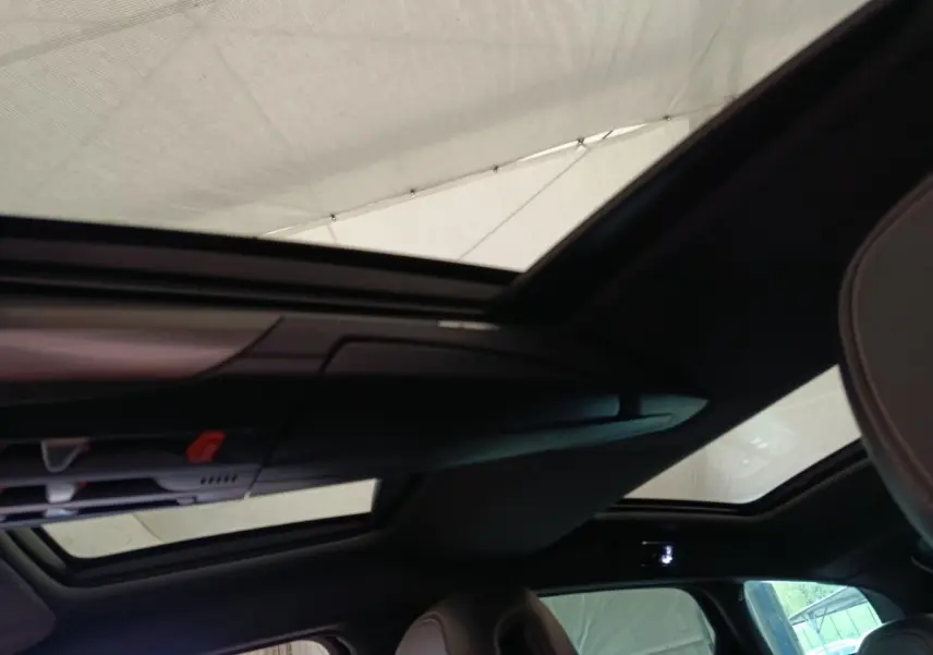 Toit panoramique ouvert vu de l'intérieur arrière d'une DS5 noire, avec sièges en cuir visibles.