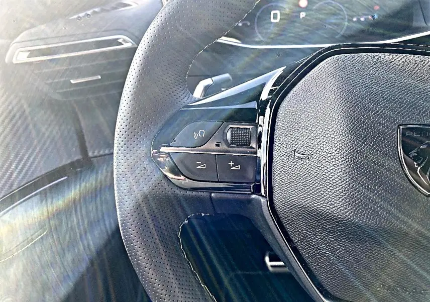 Gros plan sur le volant cuir perforé noir du Peugeot 2008 1.2 hybrid 145 GT avec commandes intégrées et tableau de bord numérique.