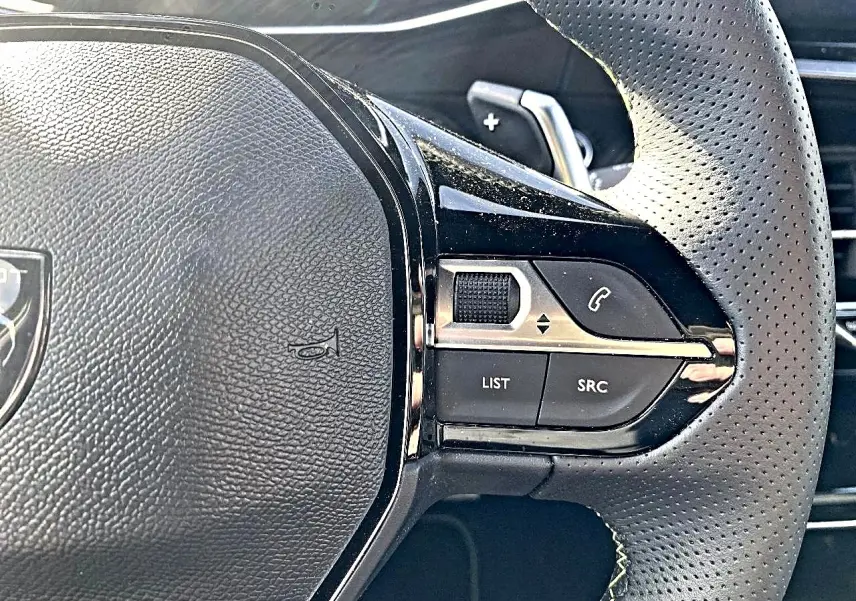 Gros plan sur le volant cuir perforé de la Peugeot 2008 1.2 hybrid 145 GT, avec commandes multifonctions à droite.