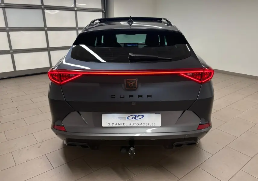 Vue arrière d'un CUPRA Formentor gris magnétique 2023 avec feux LED reliés et attelage visible en intérieur showroom.