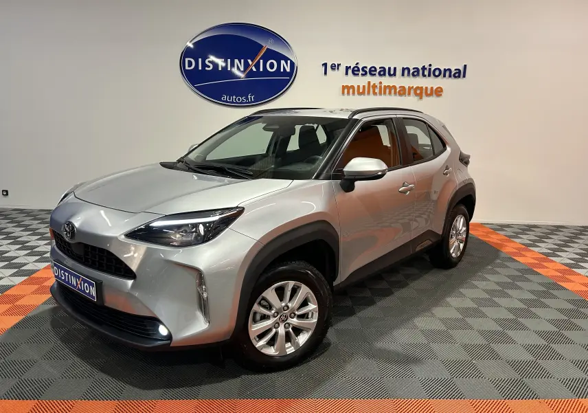 Toyota Yaris Cross gris minéral vue 3/4 avant droit en intérieur avec jantes alliage et feux allumés.