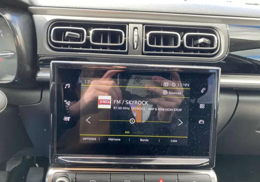 Vue rapprochée de la tablette tactile centrale de la Citroën C3 2021, affichant la radio FM Skyrock, entourée d'aérateurs noirs.