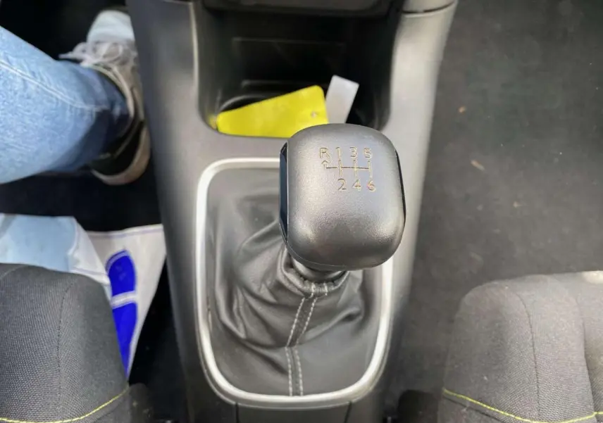 Gros plan sur le levier de vitesses manuel noir de la Citroën C3 2021, intérieur avec sièges gris et couture jaune.