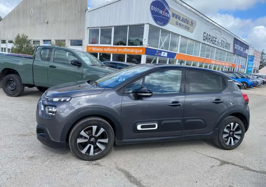 Profil droit d'une Citroën C3 gris platinium 2021 avec Airbump blanc et toit noir, stationnée devant un garage.