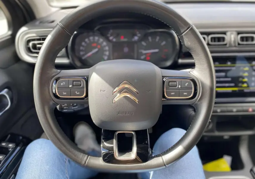 Vue centrée sur le volant noir de la Citroën C3 2021 avec tableau de bord et écran tactile en arrière-plan flou.
