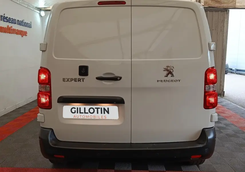 Vue arrière du Peugeot Expert Fourgon blanc 2023 avec portes battantes et feux arrière allumés en intérieur showroom.