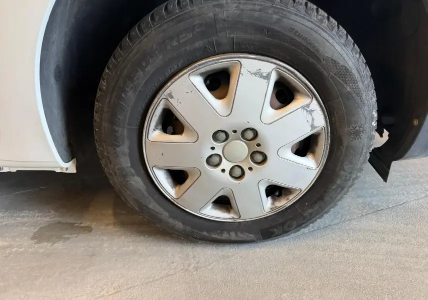 Gros plan sur la roue avant gauche d’un Renault Kangoo blanc de 2011, avec jante en acier et enjoliveur usé.
