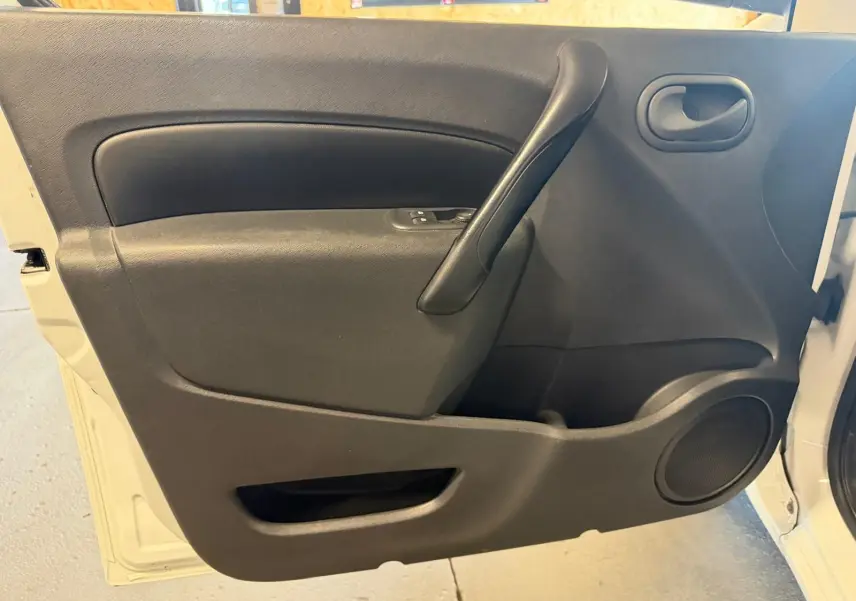 Vue intérieure de la porte avant gauche noire du Renault Kangoo blanc 2011, avec poignée et haut-parleur intégrés.