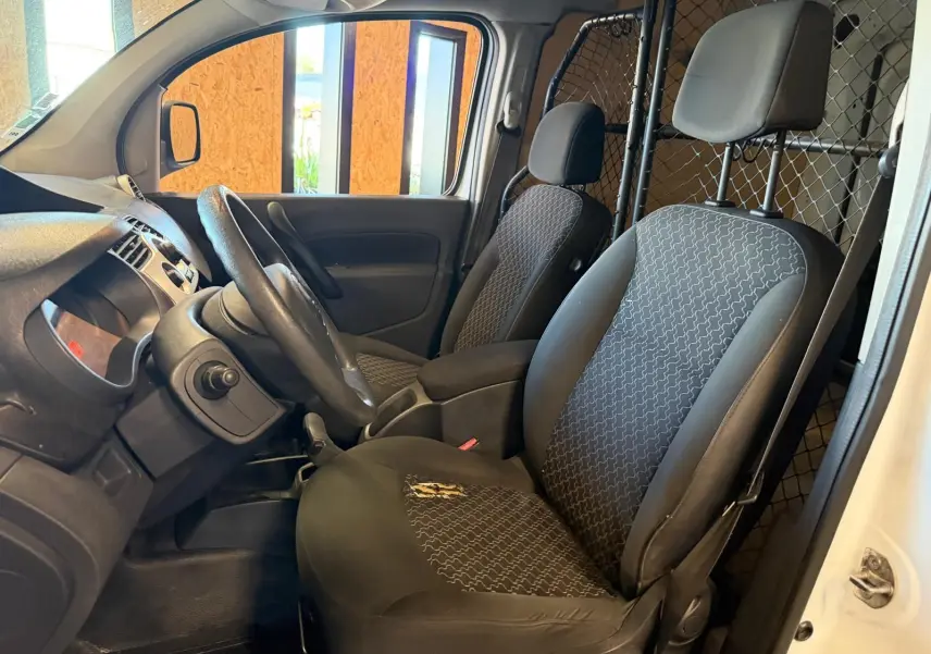 Vue intérieure côté conducteur du Renault Kangoo blanc 2011, montrant les sièges en tissu noir et la cloison métallique séparatrice.