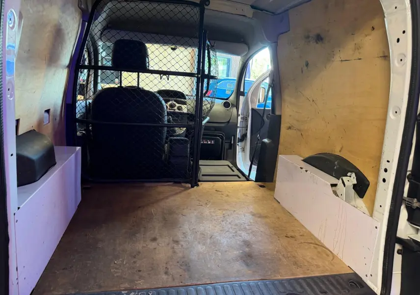 Vue intérieure arrière du Renault Kangoo blanc 2011, montrant l'espace de chargement avec cloison métallique et parois en bois.