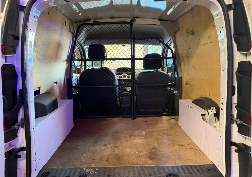 Vue intérieure arrière du Renault Kangoo blanc 2011, montrant l'espace de chargement avec cloison métallique et revêtement bois.