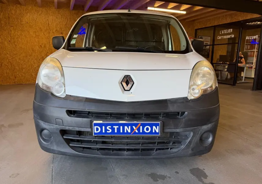 Vue frontale d’un Renault Kangoo blanc 2011 avec pare-chocs noir mat et plaque Distinxion en intérieur d’atelier.