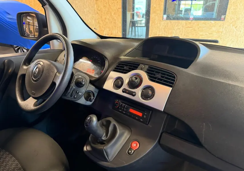 Vue intérieure côté conducteur du tableau de bord noir et volant d’un Renault Kangoo blanc avec levier de vitesse manuel.