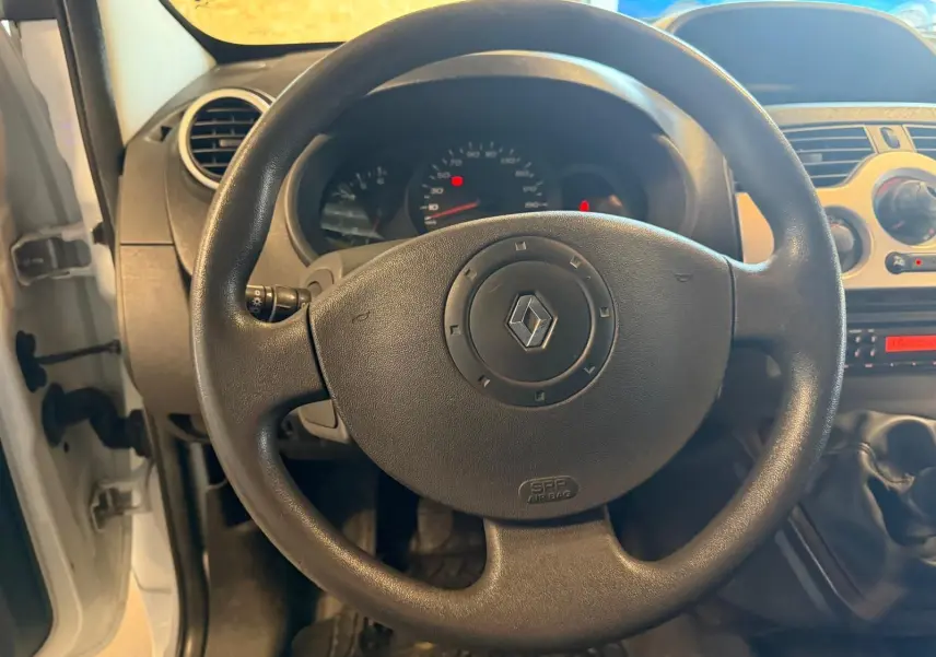 Vue intérieure centrée sur le volant noir du Renault Kangoo blanc 2011 avec tableau de bord et levier de vitesse manuel visibles.