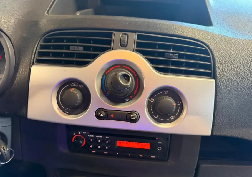 Tableau de bord intérieur du Renault Kangoo 2011, vue centrée sur les commandes de climatisation et la radio avec éclairage rouge.