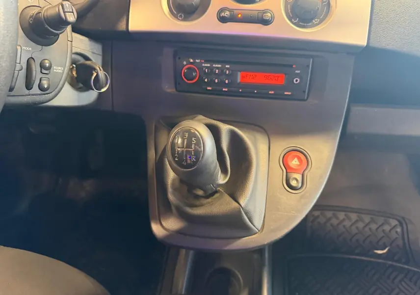 Gros plan sur le levier de vitesse manuel et la console centrale du Renault Kangoo blanc, avec radio et bouton de warning rouge.