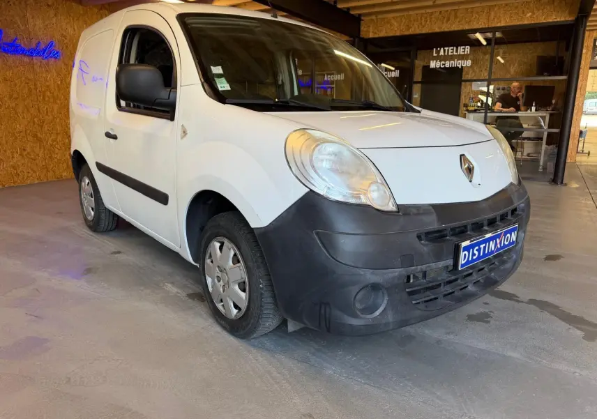 Vue 3/4 avant gauche d’un Renault Kangoo blanc de 2011 avec pare-chocs noir et plaque Distinxion en intérieur d’atelier.