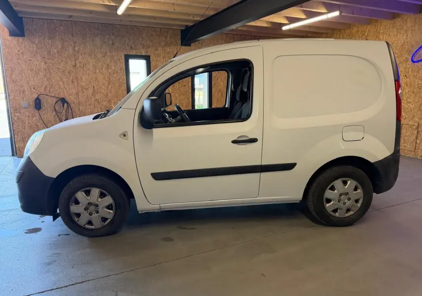 Vue de profil côté gauche d’un utilitaire Renault Kangoo blanc 2011 avec porte latérale pleine, stationné en intérieur.