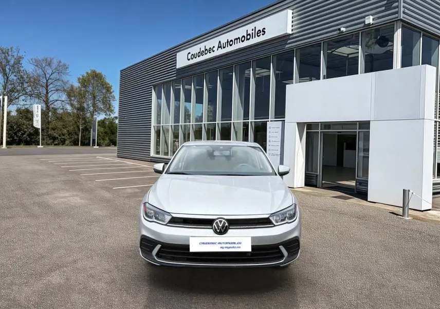 Vue avant d'une Volkswagen Polo grise 2025 stationnée devant un bâtiment moderne de concession automobile.