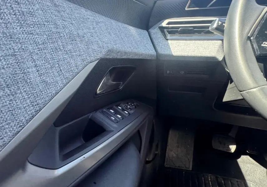 Vue intérieure côté gauche du Peugeot 3008 Hybrid 136 e-DCS6 Allure 2025, montrant la portière avec commandes et tissu gris.