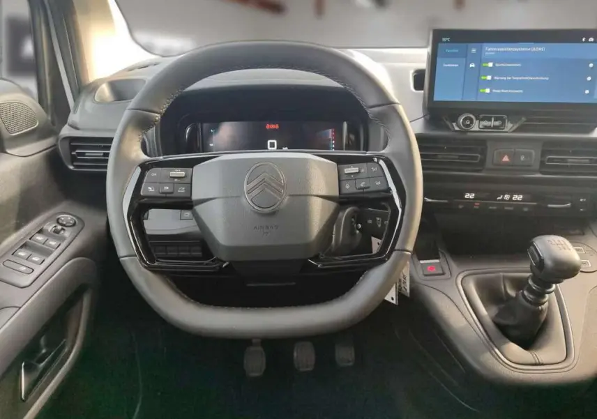 Vue intérieure centrée sur le volant cuir multifonctions et levier de vitesse manuel du Citroën Berlingo gris Artense.