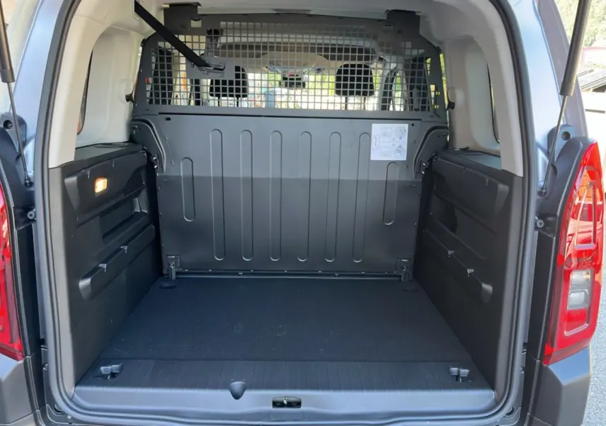 Coffre ouvert d’un Citroën Berlingo BlueHDi 100 Feel Plus gris Artense, avec grille de séparation et espace de chargement vide.