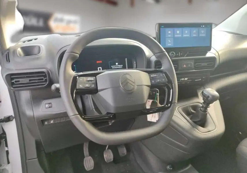 Vue intérieure centrée sur le volant cuir multifonctions et la console avec écran tactile du Citroën Berlingo gris Artense.