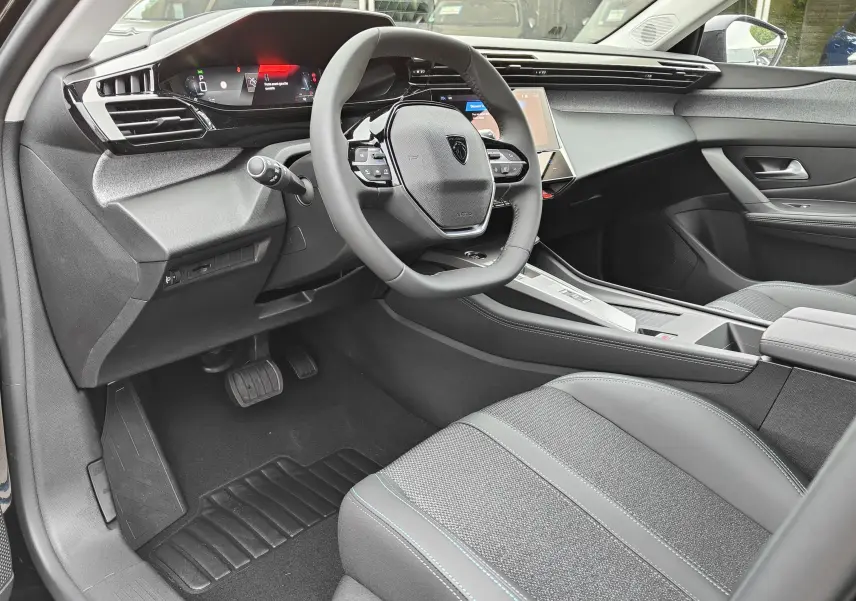 Vue intérieure côté conducteur de la Peugeot 308 PureTech 130 Allure Pack 2023, tableau de bord moderne et sièges gris.