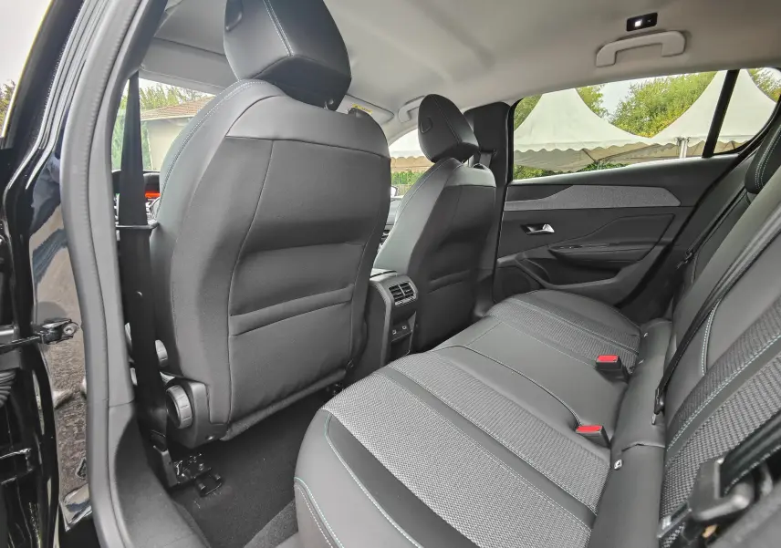 Vue intérieure arrière côté droit de la Peugeot 308 PureTech 130 Allure Pack 2023 noire, sièges en tissu et cuir avec surpiqûres bleues.