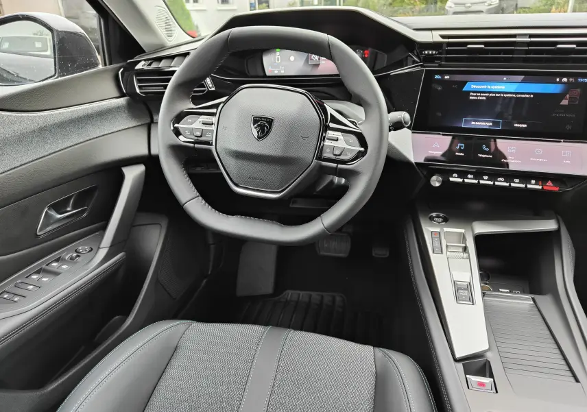 Vue intérieure centrée sur le volant compact et la console centrale moderne de la Peugeot 308 PureTech 130 Allure Pack noire 2023.