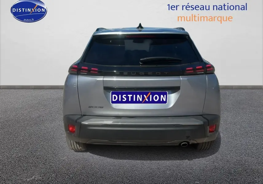 Vue arrière d'un Peugeot 2008 gris artense avec feux LED et lunette arrière surteintée, en extérieur sur sol goudronné.
