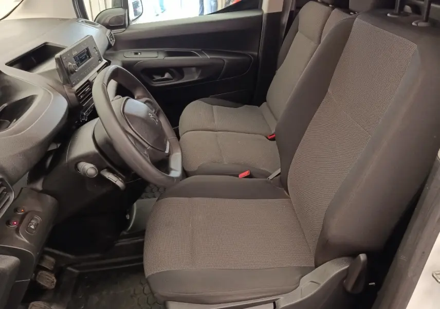 Vue intérieure côté conducteur du Peugeot Partner 2022 blanc, montrant le volant et les sièges avant gris foncé.