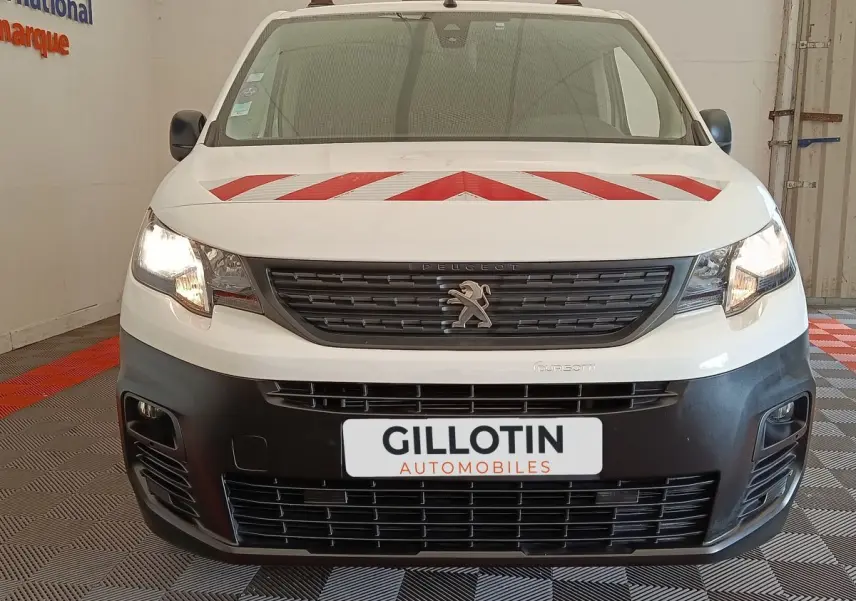 Vue avant d’un Peugeot Partner blanc 2022 avec marquage rouge sur le capot et phares allumés en intérieur.