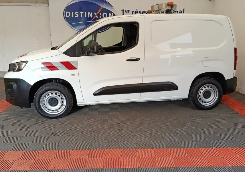 Vue de profil côté gauche d’un Peugeot Partner blanc utilitaire avec bandes rouges réfléchissantes sur l’aile avant.