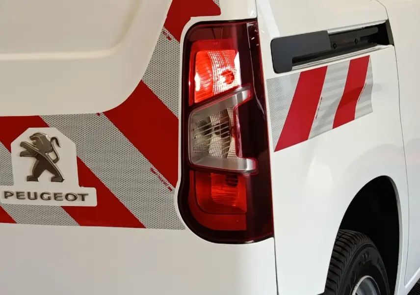Gros plan sur l'arrière droit blanc du Peugeot Partner 2022 avec bandes rouges réfléchissantes et feu arrière allumé.