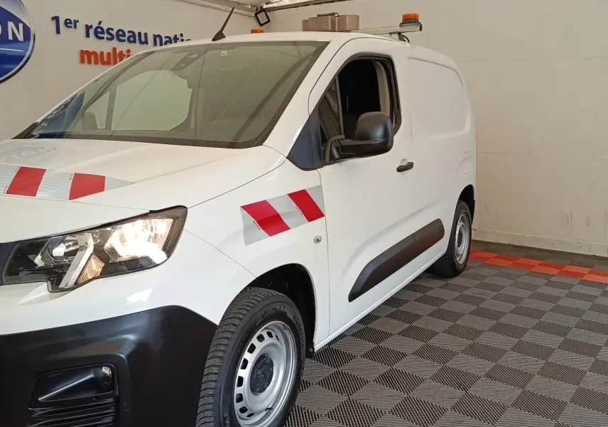 Vue 3/4 avant droite d’un Peugeot Partner blanc avec bandes réfléchissantes rouges et grises sur l’aile et le capot.