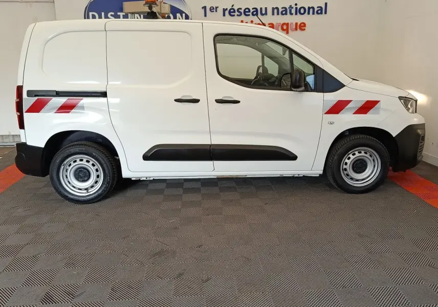 Vue de profil côté droit d’un utilitaire Peugeot Partner blanc avec bandes réfléchissantes rouges et jantes acier.
